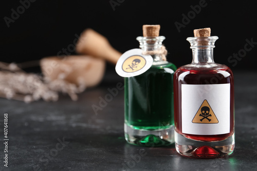 Glass bottles of poisons with warning signs on black table. Space for text