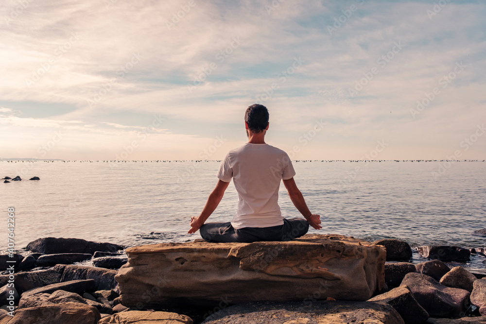 Naklejka premium Attractive young man practicing yoga meditation and breathwork outdoors by the sea
