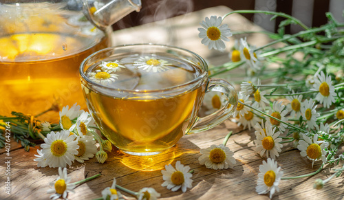 Glass of herbal chamomile tea and chamomile flowers on wooden table.