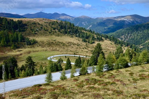 Alpine road called Nockalmstrasse (Nockalm Road) in Kaernten (Carinthia), Austria, mountain range of Nockerberge (Nocky Mountains) on horizon, sunny autumn landscape, blue sky with clouds background
 photo