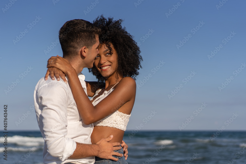 Multiracial young couple embracing on the beach Multiracial young couple embracing on the beach