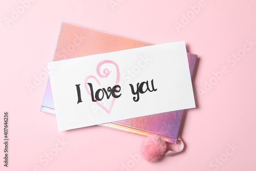 Card with text I Love You and shiny notebook on pink background, top view