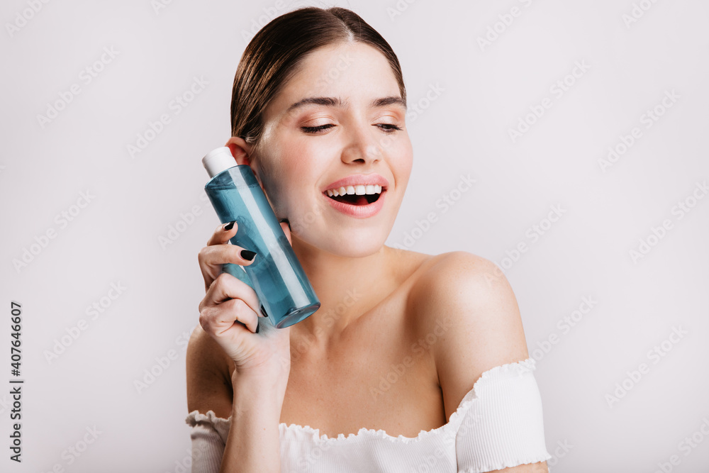 Closeup portrait of cute girl without makeup holding blue bottle with healing tonic for face skin Closeup portrait of cute girl without makeup holding blue bottle with healing tonic for face skin