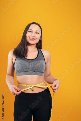 A slender woman measures her waist with a measuring tape. n a yellow background. photo