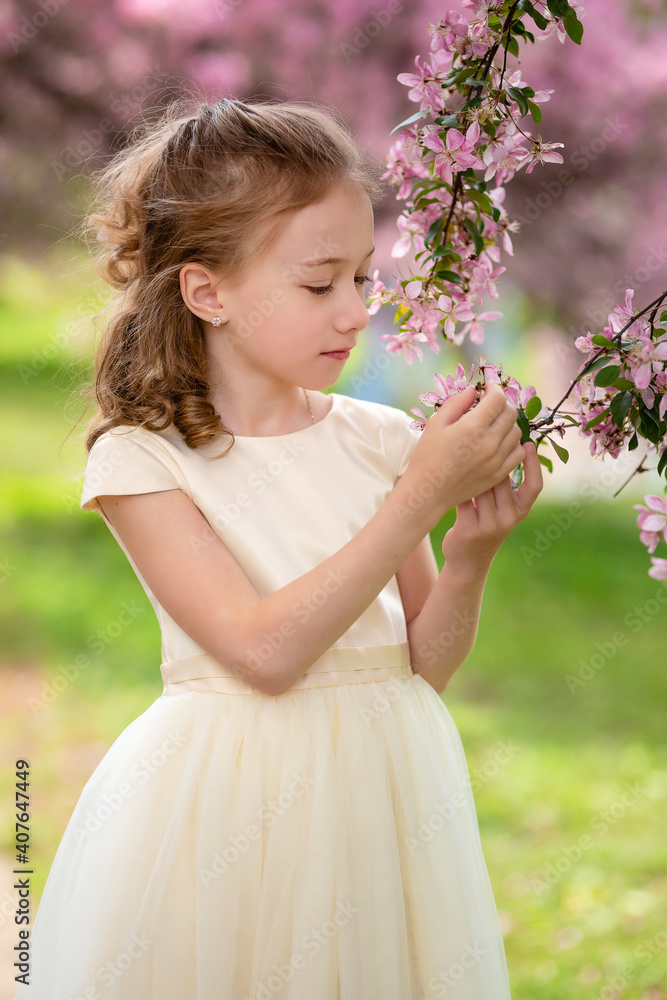 Cute little pensive girl with handmade hair wreath on her head smelling flowers in the spring blossom garden, close-up Cute little pensive girl with handmade hair wreath on her head smelling flowers in the spring blossom garden, close-up