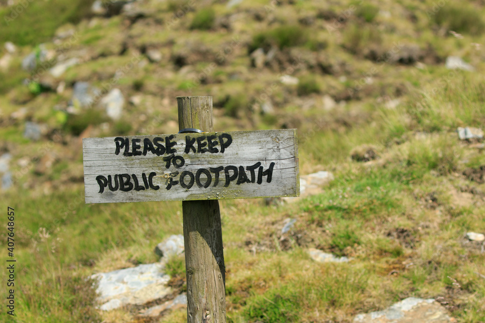 Old wooden please keep to the public footpath signpost in a rocky field.