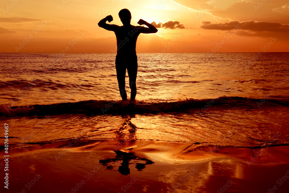 Silhouette of a man in swimming trunks standing in the water near the sea at sunrise. Positioning a healthy lifestyle. A cheerful mood and a lifted body.