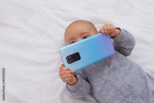 Newborn baby holding smartphone in hands in front of face
