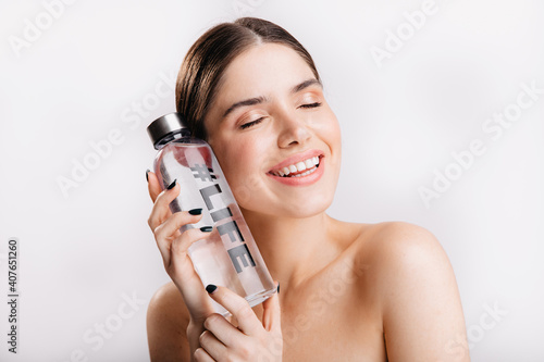 Adorable girl without makeup posing with bottle of water on isolated background. Smiling model demonstrates importance of water for life