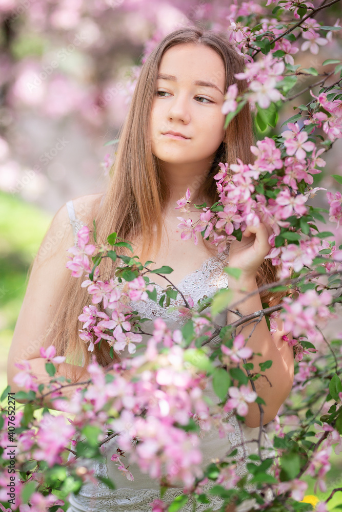 Cute little pensive girl with handmade hair wreath on her head smelling flowers in the spring blossom garden, close-up Cute little pensive girl with handmade hair wreath on her head smelling flowers in the spring blossom garden, close-up