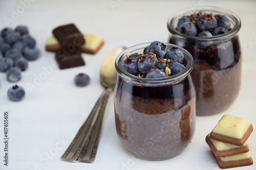 Chia seed pudding, super food healthy chia dessert with cocoa, bluberries and chocolate  on white wooden background