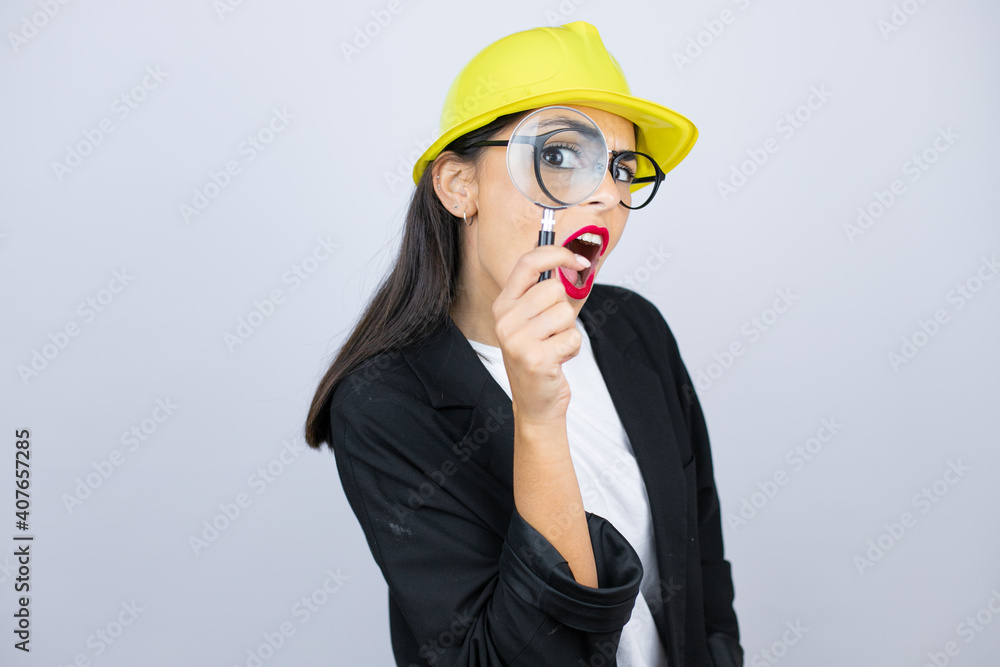 Young architect woman wearing hardhat looking through a magnifying glass Young architect woman wearing hardhat looking through a magnifying glass