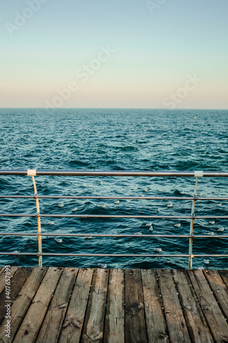 Old wooden rustic pier with metal handrail. Blue cold sea view skyline. Winter seascape. Central composition. Concept of enjoying nature, nobody, loneliness, freedom, tranquility, dreaming, thinking