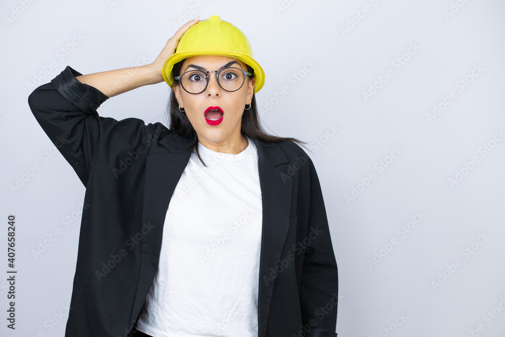 Young architect woman wearing hardhat putting one hand on her head smiling like she had forgotten something