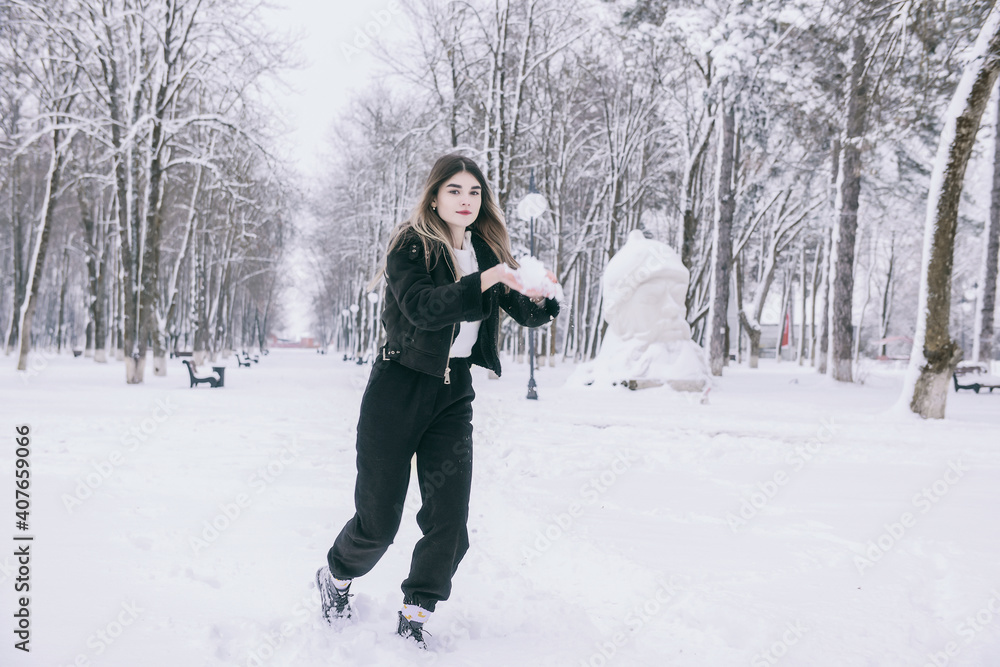A beautiful young girl in warm clothes walks, plays and poses against the background of a winter snow-covered park and a playground A beautiful young girl in warm clothes walks, plays and poses against the background of a winter snow-covered park and a playground