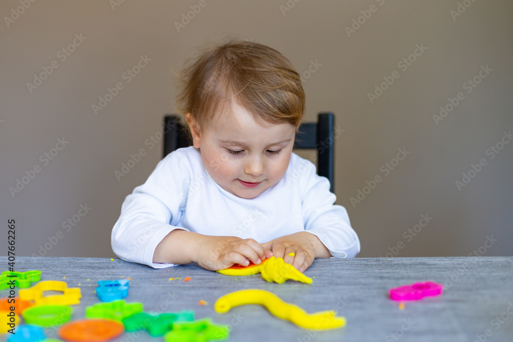 little child playing with placticine, dough, colorful modeling compound, sitting at table at home or kindergarten. Creative leisure with kids.