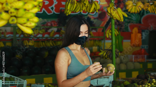 European girl in a black protective mask buys organic fruits in a store