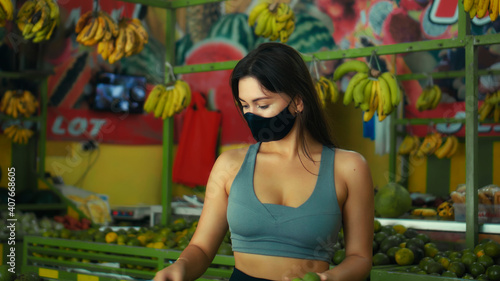 European girl in a black protective mask buys organic fruits in a store