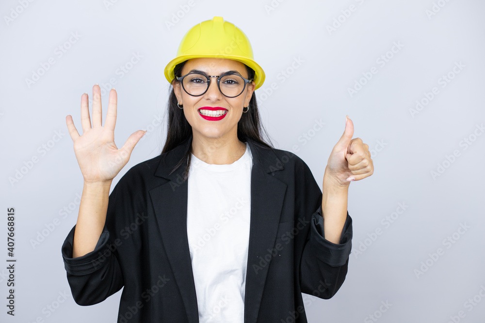 Young architect woman wearing hardhat showing and pointing up with fingers number six while smiling confident and happy Young architect woman wearing hardhat showing and pointing up with fingers number six while smiling confident and happy