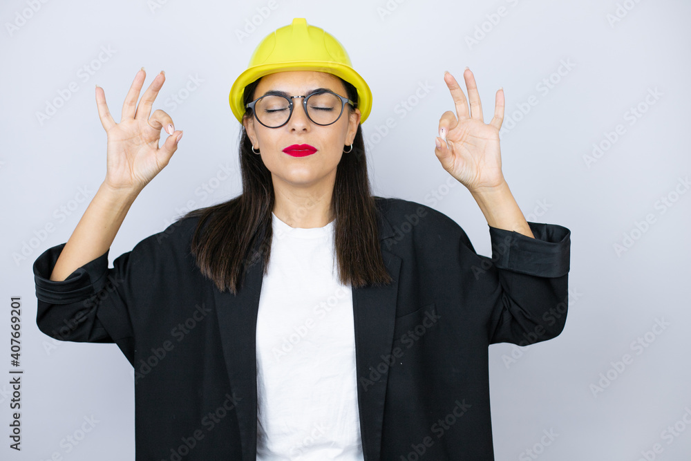 Young architect woman wearing hardhat relax and smiling with eyes closed doing meditation gesture with fingers Young architect woman wearing hardhat relax and smiling with eyes closed doing meditation gesture with fingers