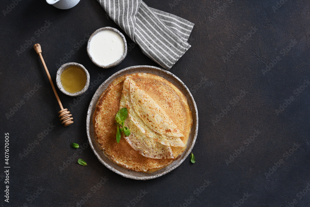 Thin pancakes with sour cream and honey on a dark concrete background. A stack of pancakes. View from above. Thin pancakes with sour cream and honey on a dark concrete background. A stack of pancakes. View from above.