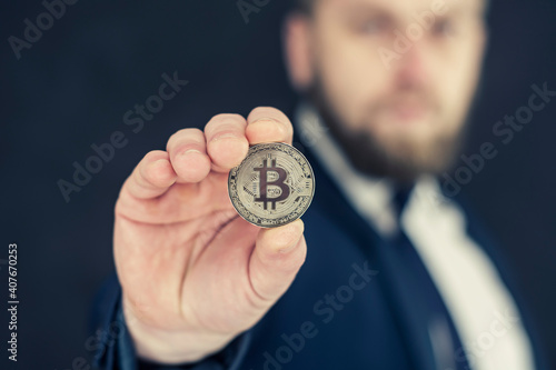 A businessman in a blue jacket holding Bitcoin in his hands. Virtual currency and blockchain concept.