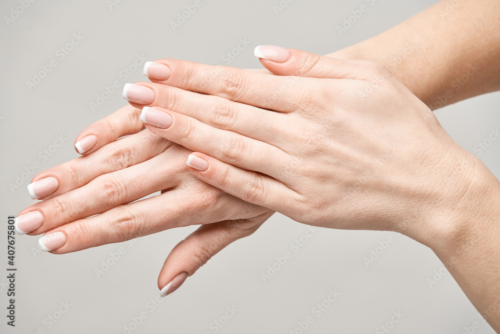 Beautiful Female Hands with French manicure over light grey background