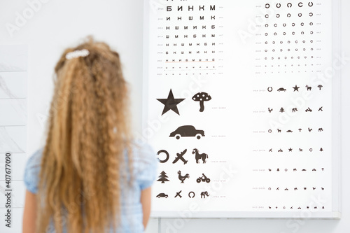 medicine, health and eyevision concept. Close up rear view of little girl looking at eye test chart. photo
