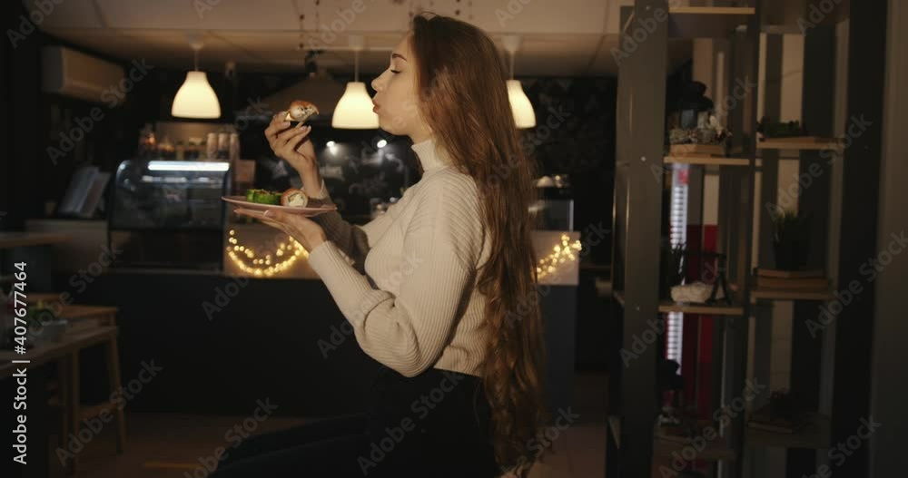 Sensual young girl with very long blond hair sits on a table in a cafe and eats sushi with chopsticks throwing her head back Sensual young girl with very long blond hair sits on a table in a cafe and eats sushi with chopsticks throwing her head back