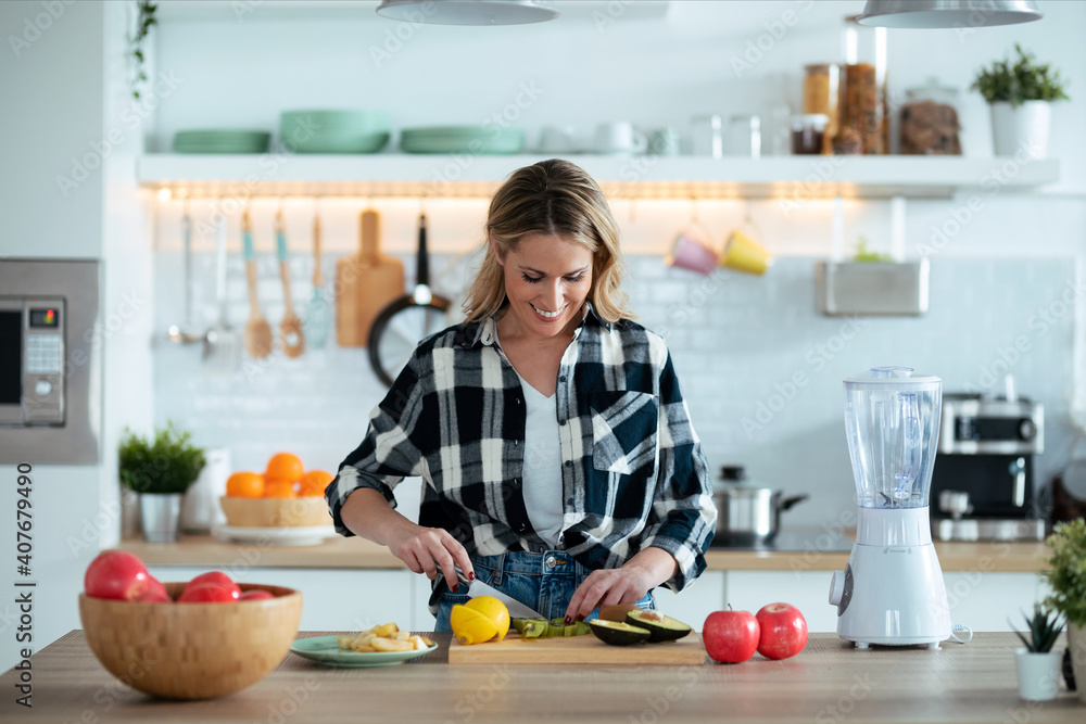 Pretty mature woman cutting fruit while preparing detox drink in the kitchen at home. Pretty mature woman cutting fruit while preparing detox drink in the kitchen at home.