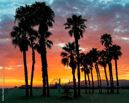 Beautiful and colorful sunset on the Santa Monica beach, with the palm trees and the Pacific Park Amusement Park on the Santa Monica pier darkened against the vibrant sky.