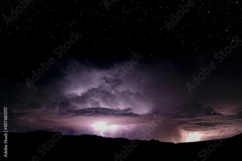 Powerful lightning storm in the American Southwest. One sees the silhouette of the hills on bottom, and moving up from there the lightning, cumulonimbus and the starry sky above. 