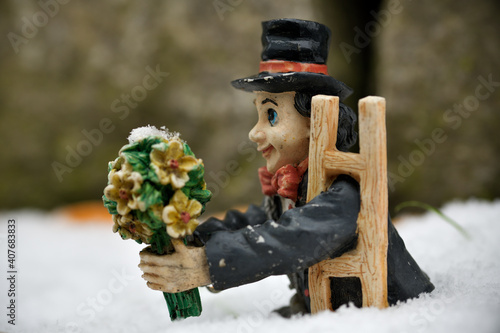 Eine Schornsteinfegerfigur steht im Schnee und reicht einen Blumenstrauß
