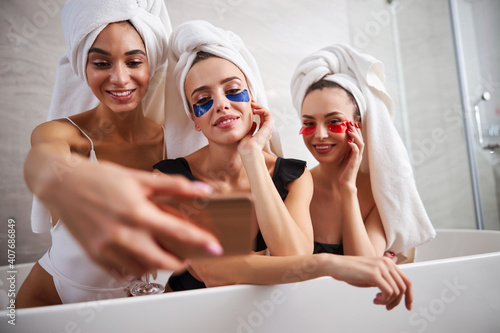 Three young women smiling while taking photos in a bathtub