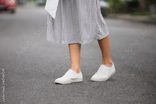 woman in white leather shoes and striped grey skirt is walking on the road outside