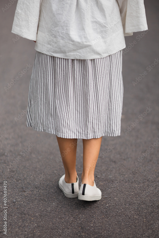 woman in white leather shoes and striped grey skirt is walking on the road outside woman in white leather shoes and striped grey skirt is walking on the road outside