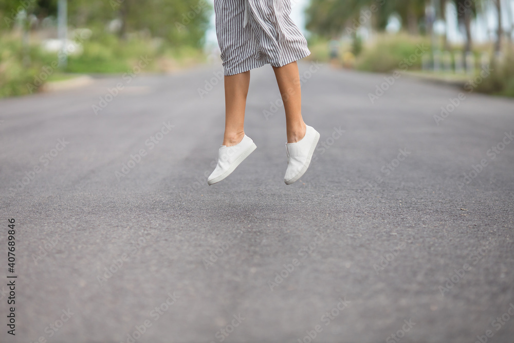 woman in white leather shoes and striped grey skirt is jumping on the road outside woman in white leather shoes and striped grey skirt is jumping on the road outside