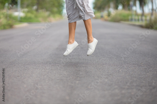 woman in white leather shoes and striped grey skirt is jumping on the road outside