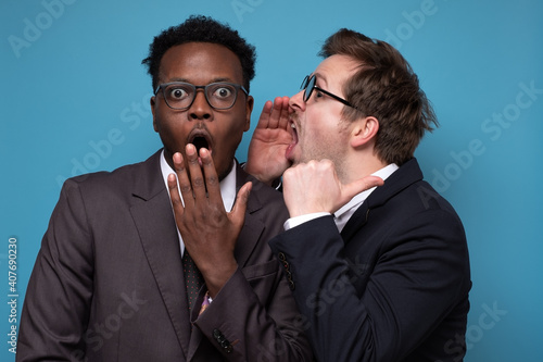 Fotografie Caucasian man whispering to his african coworker ear telling him something secret