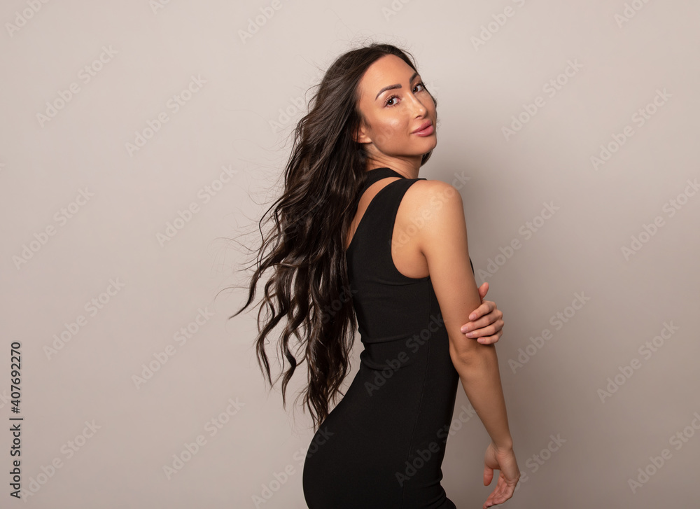 Beautiful young woman with long shiny black hair and natural make-up posing in dress on grey background Beautiful young woman with long shiny black hair and natural make-up posing in dress on grey background