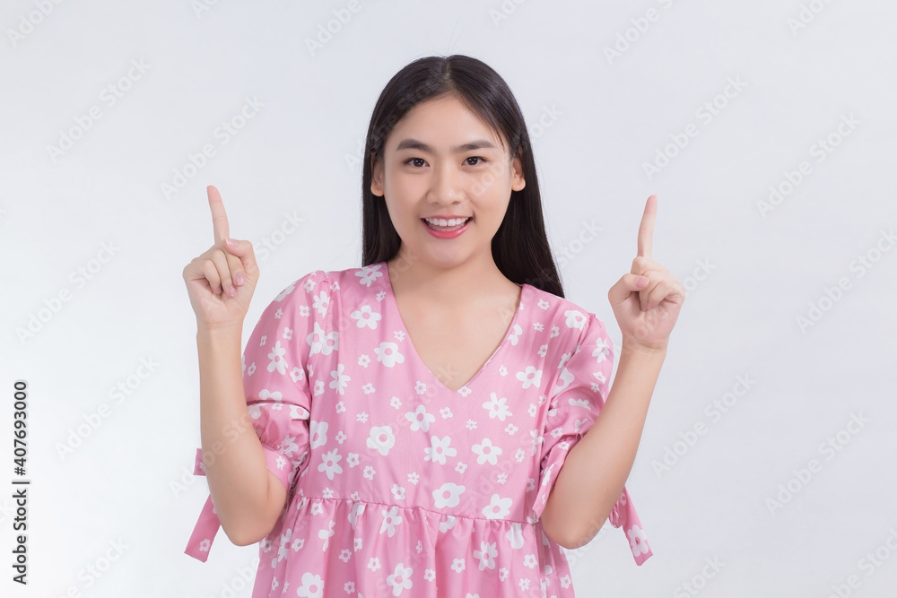 Asian beautiful woman with black long hair wears pink dress and point up to present something on the white background. Asian beautiful woman with black long hair wears pink dress and point up to present something on the white background.