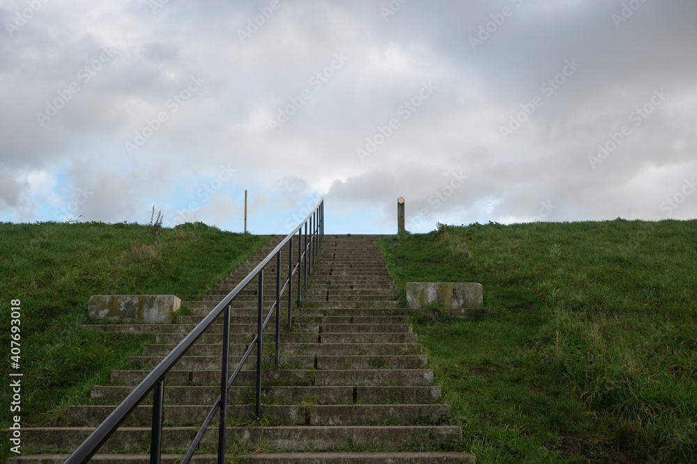 Concrete staircase on a dike with an iron railing in the middle and a cloudy sky