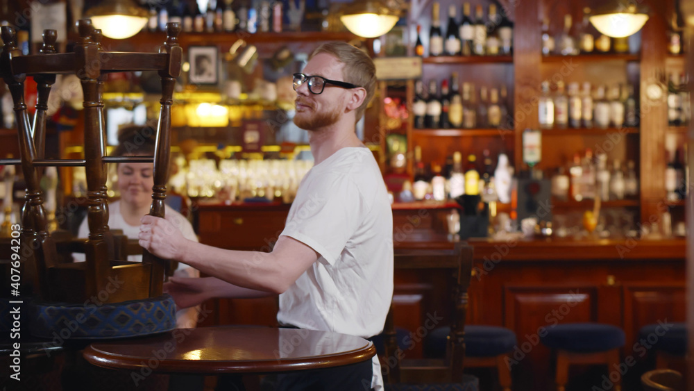 Waiters in modern pub putting furniture down preparing for opening Waiters in modern pub putting furniture down preparing for opening