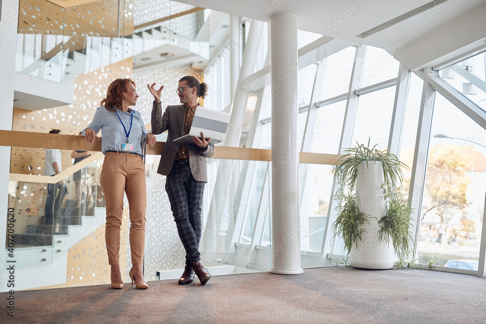 Obraz premium young man explaining to older female colleague standing in the hallway of a business building