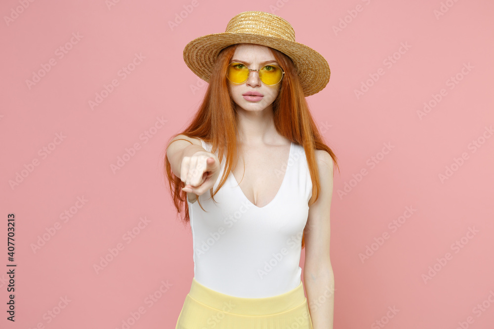 Young serious strict redhead woman 20s ginger long hair wear straw hat glasses summer clothes pointing index finger camera on you opened mouth isolated on pastel pink color background studio portrait. Young serious strict redhead woman 20s ginger long hair wear straw hat glasses summer clothes pointing index finger camera on you opened mouth isolated on pastel pink color background studio portrait.