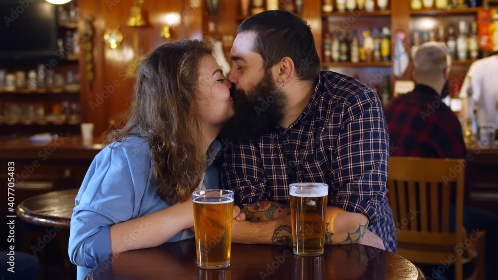 Woman and man celebrating drinking golden craft beer sitting at wooden table indoors at pub