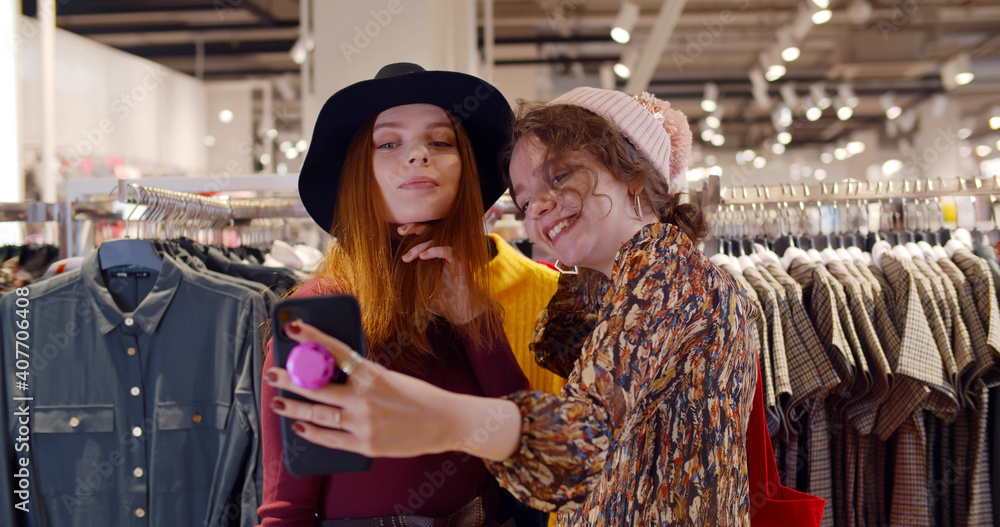 Young beautiful ladies wearing hats taking selfie while shopping in clothing store. Young beautiful ladies wearing hats taking selfie while shopping in clothing store.