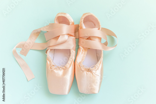 New pastel beige ballet shoes with satin ribbon isolated on blue background. Ballerina classical pointe shoes for dance training. Ballet school concept. Top view flat lay, copy space