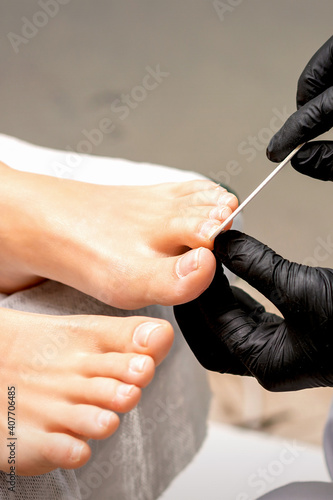 Pedicure master s hands in protective rubber gloves file female toenails with a nail file in a beauty salon