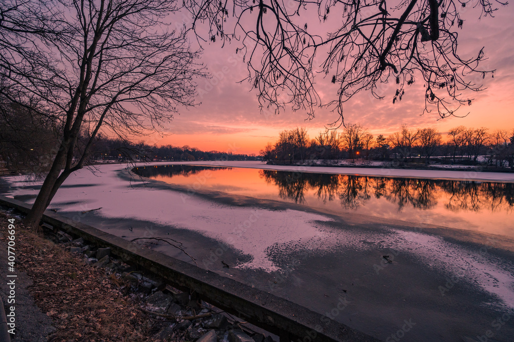 Colourful sunset over frozen lake in city park during cold winter evening